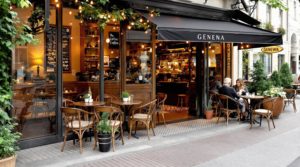 Cozy Geneva café interior with elegant wooden furniture and warm golden tones. A specialty coffee featuring intricate latte art is in focus, surrounded by stylish patrons enjoying the inviting atmosphere under soft ambient lighting. The vintage-design cozy café also includes a charming terrace setting.