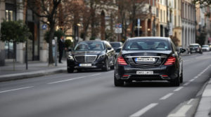 A professional scene showing chauffeurs in tailored suits driving 2024 black Mercedes S-Class vehicles with 'SWISS LIM CO' white license plates along a quiet urban road in Geneva, embodying a refined atmosphere ideal for airport transfer VTC Geneva services.