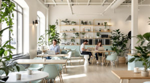 Stylish coworking space in Geneva with young professionals working on laptops. The bright, airy interior features minimalistic decor with natural materials, light grey walls, and fresh mint furniture. Coffee cups are on tables, and soft natural lighting creates an inviting cowork