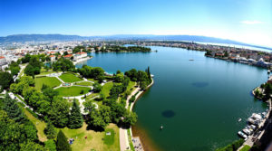 A wide-angle view of Lake Geneva featuring lush green parks and serene lakesides, with people strolling, picnicking, and enjoying nature under a clear blue sky, illustrating the peaceful atmosphere and beauty of outdoor activities, including various lake geneva walk types